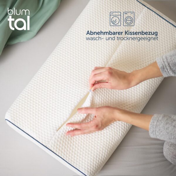 Hände, die den Bezug eines weißen strukturierten Kissens auf einem Bett öffnen, mit deutschem Text, der darauf hinweist, dass der Bezug abnehmbar und maschinenwaschbar ist. Hände, die den Bezug eines weißen strukturierten Kissens auf einem Bett öffnen, mit deutschem Text, der darauf hinweist, dass der Bezug abnehmbar und maschinenwaschbar ist.